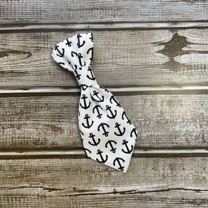 May include: A white bow tie with a black anchor pattern. The bow tie is on a wooden background.
