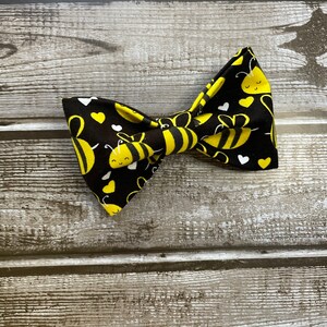 May include: A black bow tie with a yellow and white bee pattern and white hearts.