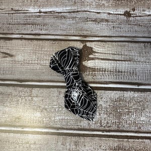 May include: Black bow tie with a white spiderweb pattern. The bow tie is on a wooden background.