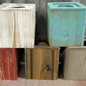 May include: Five wooden tissue box covers in various colors, including white, teal, red, brown, and gray. The boxes are stacked on top of each other, with the white box on top and the gray box on the bottom.