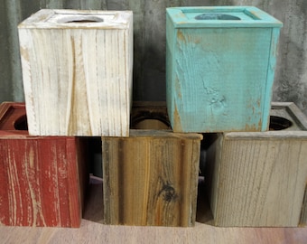 May include: Five wooden tissue box covers in various colors, including white, teal, red, brown, and gray. The boxes are stacked on top of each other, with the white box on top and the gray box on the bottom.