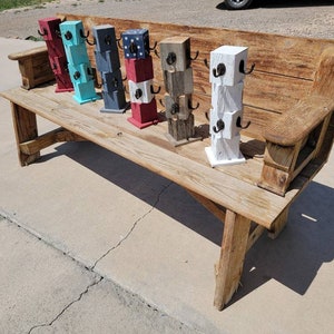 May include: A collection of wooden mug racks in various colors, including red, blue, and white, with black hooks. The racks are displayed on a rustic wooden bench. Each rack is made of stacked blocks.