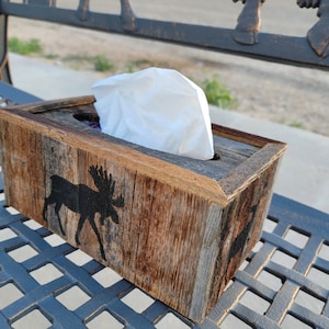 May include: A rustic wooden tissue box holder with a moose silhouette design. The box is made of reclaimed wood and has a natural, weathered finish.