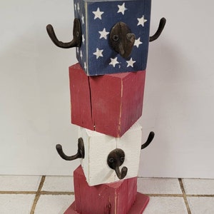 May include: A wooden stand with three tiers painted in red, white, and blue with a stars and stripes pattern. Each tier has two metal hooks.
