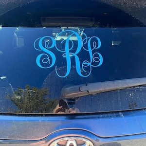 May include: A blue monogram decal with the letters "S R E" on a dark blue car window.
