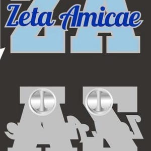 May include: A metal lapel pin featuring the light blue block letters ZA with the text Zeta Amicae in blue script layered over them. The reverse side of the pin is silver-colored with two circular metal pin back fasteners attached to the letters.