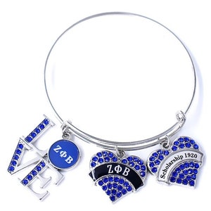 May include: A silver charm bracelet with blue and black charms. The charms include a heart with the letters "ZΦB" and a heart with the text "Scholarship 1920". The bracelet also has a charm with the letters "LOVE" and a charm with the letters "ZΦB".