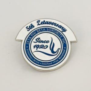 May include: A white and blue enamel pin with the text "5th Zetaversary Zeta Phi Beta Sorority Inc. Since 1920" and a stylized dove design.