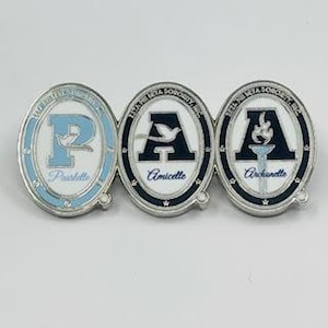 May include: Three oval-shaped pins connected together. Each pin features a different design with the letters "P", "A", and "A" in blue and white. The pins are silver-toned with blue and white enamel detailing and the words "Pearllette", "Amicette", and "Archanette".