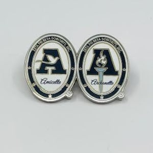 May include: Two oval-shaped pins with a white background and a black outline. The pins feature a black letter "A" with a white dove on the left pin and a white torch on the right pin. The text "Alpha Delta Sorority, Inc." is written around the top of each pin. The text "Amicelle" is written below the dove on the left pin and "Ardiente" is written below the torch on the right pin.
