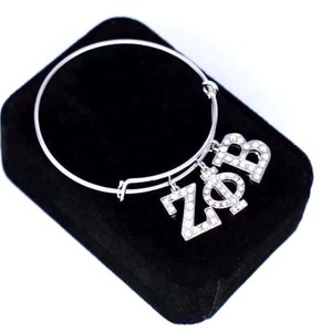 May include: A silver bangle bracelet with a charm that says "ZΦB" in rhinestones.