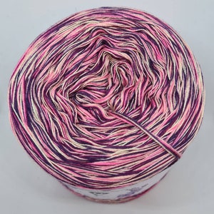 May include: A skein of yarn with a pink, purple, and cream color gradient. The yarn is wound into a ball shape and is ready to be used for knitting or crocheting.