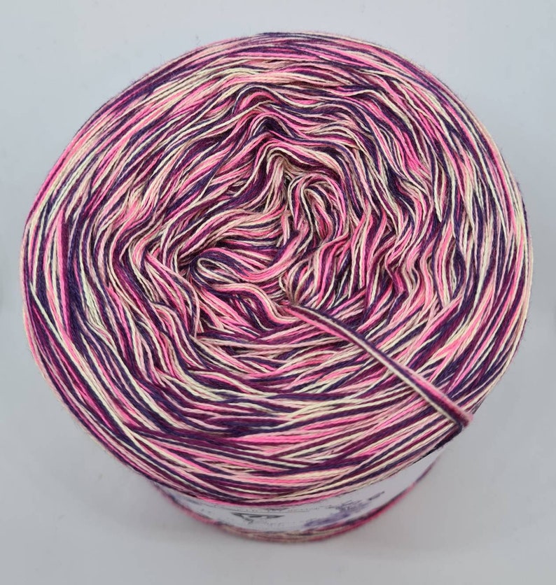 May include: A skein of yarn with a pink, purple, and cream color gradient. The yarn is wound into a ball shape and is ready to be used for knitting or crocheting.