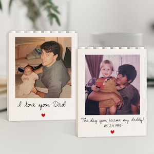 May include: Two white photo blocks with Polaroid-style images. One shows a man holding a baby, with the text "I love you Dad" and a red heart. The other shows a man and child, with the text "The day you became my daddy! 05.24.1995" and a red heart.
