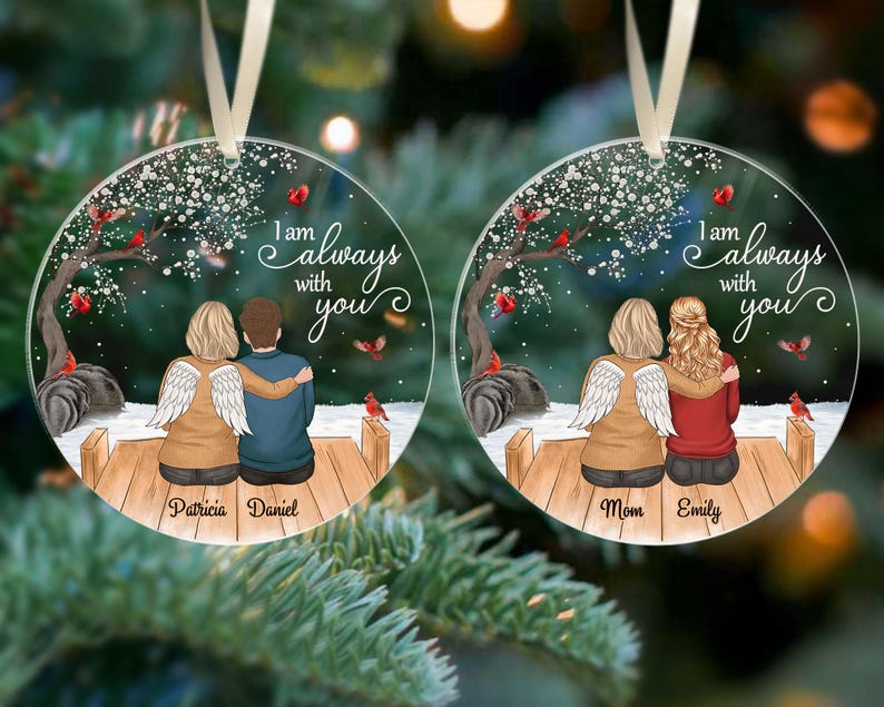 Puede incluir: Dos adornos navide&ntilde;os redondos y transparentes con un dise&ntilde;o impreso. Cada adorno presenta a una pareja sentada en un muelle de madera bajo un &aacute;rbol con p&aacute;jaros rojos. El texto "I am always with you" est&aacute; escrito en cada adorno. Un adorno dice "Patricia Daniel" y el otro dice "Mom Emily".