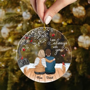Puede incluir: Un adorno navide&ntilde;o redondo y transparente con un colgador dorado. El adorno presenta una pareja con alas de &aacute;ngel, un &aacute;rbol y el texto "I am always with you". Tambi&eacute;n se incluyen los nombres "Mom" y "Daniel".