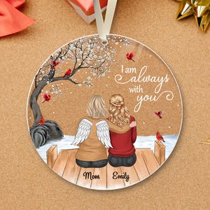 Puede incluir: Adorno redondo con una conmovedora escena de dos figuras abraz&aacute;ndose en un muelle, con un &aacute;rbol y cardenales. Se muestra el texto "I am always with you". El adorno tiene una cinta blanca para colgar.