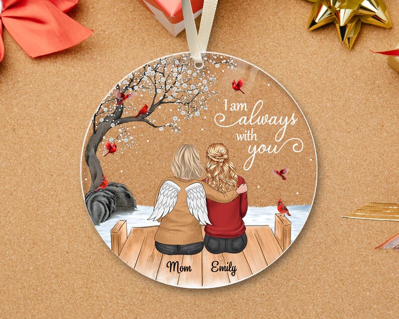 Puede incluir: Adorno redondo con una conmovedora escena de dos figuras abraz&aacute;ndose en un muelle, con un &aacute;rbol y cardenales. Se muestra el texto "I am always with you". El adorno tiene una cinta blanca para colgar.