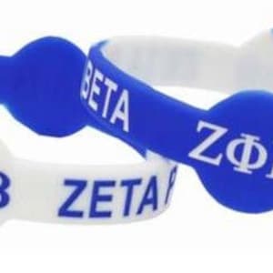 Puede incluir: Dos pulseras de silicona azul y blanca con el texto "Zeta Phi Beta" en ellas. Las pulseras están diseñadas con un fondo blanco y letras azules.