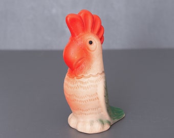 May include: A vintage rubber toy bird with a red crest, white body, and green tail feathers. The bird is a cockatoo or parrot.