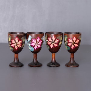 Op de afbeelding: Vier houten shotglazen met geschilderde bloemenmotieven. De glazen zijn bruin met roze, blauwe en groene bloemen.