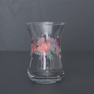 May include: A clear glass teacup with a floral design. The design features pink, purple, and green flowers.
