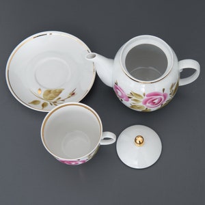 May include: A white porcelain tea set with a floral design. The set includes a teapot, a teacup, a saucer, and a lid. The teapot has a gold trim and a pink rose design. The teacup and saucer have a gold trim and a pink rose design.