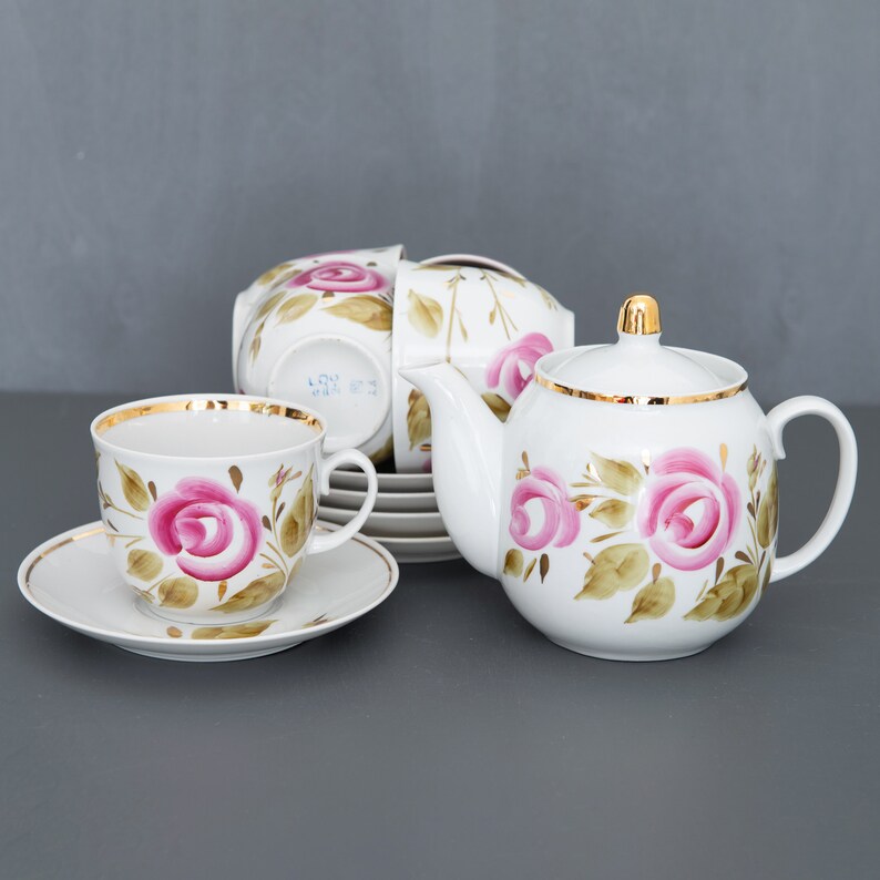 May include: A white porcelain tea set with a pink rose floral design and gold trim. The set includes a teapot, cups, and saucers.