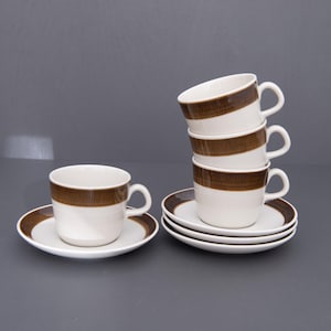 May include: A collection of white ceramic teacups and saucers. Each cup features a brown band and a matching brown rim on the saucer. Four cups are stacked, with two cups and saucers arranged on a grey surface.