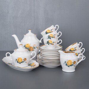 May include: A white porcelain tea set with a yellow and green floral pattern. The set includes a teapot, sugar bowl, creamer, and six cups and saucers.