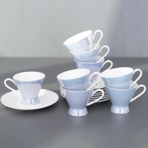 Puede incluir: Un juego de seis tazas de té y platillos de porcelana azul y blanca. Las tazas están apiladas en forma de pirámide, con los platillos debajo.