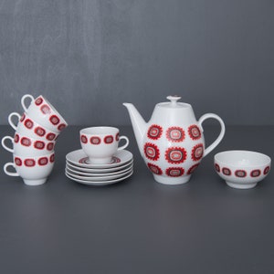 Op de afbeelding: Een witte theepot en theekopjes met een rood-wit geometrisch patroon. De set bevat een theepot, vier kopjes, vier schoteltjes en een suikerpot.