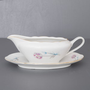 May include: A white porcelain gravy boat with a gold rim and a floral design. The boat is on a matching saucer.