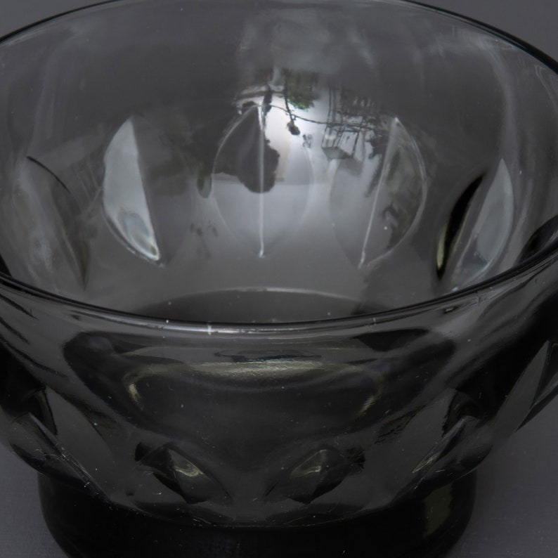May include: A dark grey glass bowl with a textured, faceted design. The bowl is empty and has a reflective surface.