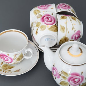 May include: A white porcelain tea set with a gold trim and floral design. The set includes a teapot, four teacups, and saucers. The flowers are pink and green.