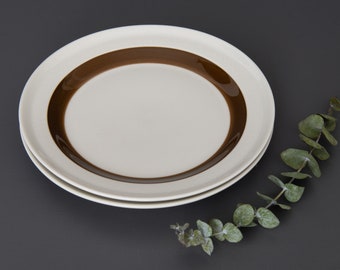 May include: A white ceramic plate with a brown band around the edge. The plate is stacked on top of another similar plate.