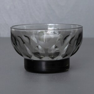 May include: A small, clear glass bowl with a black base. The bowl has a textured, patterned design.