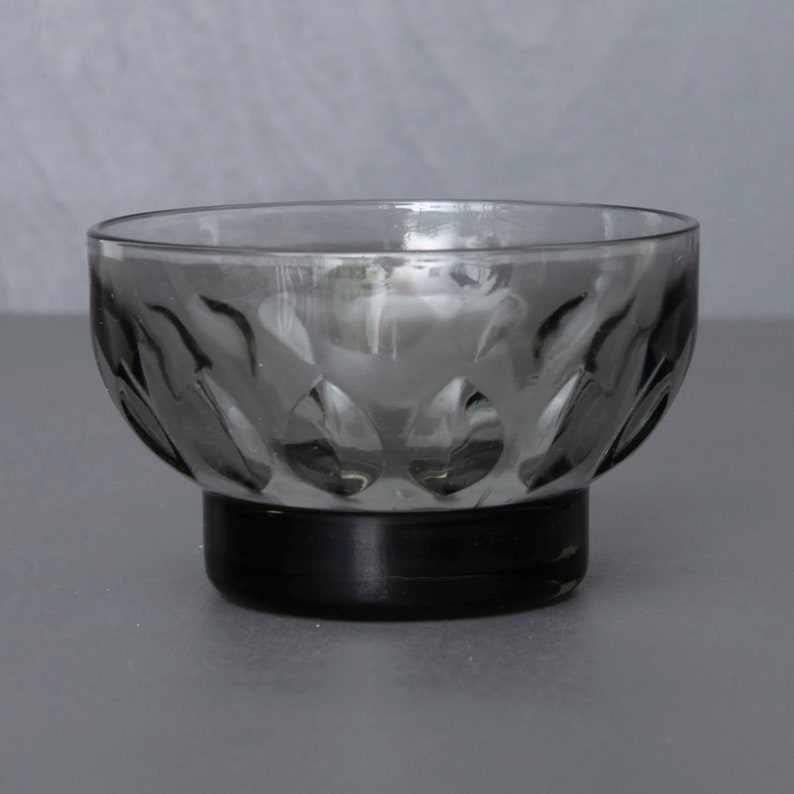 May include: A small, clear glass bowl with a black base. The bowl has a textured, patterned design.