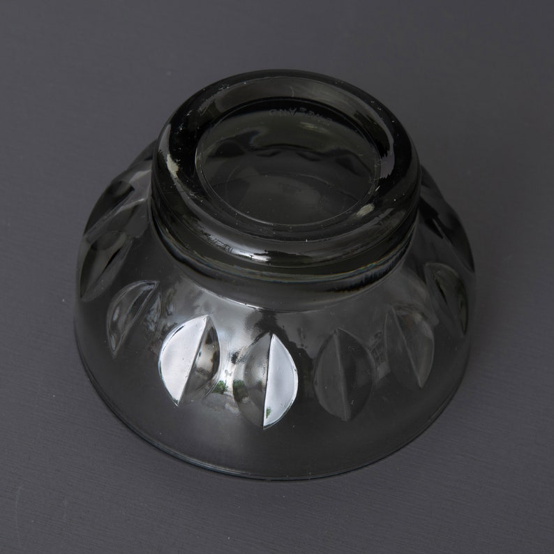 May include: A dark grey glass bowl with a decorative pattern of leaves around the rim. The bowl is empty and has a smooth, reflective surface.