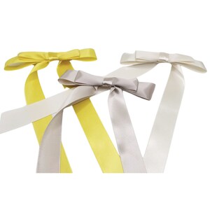 May include: Three satin ribbon bows in yellow, grey, and white. The bows are tied with long tails.