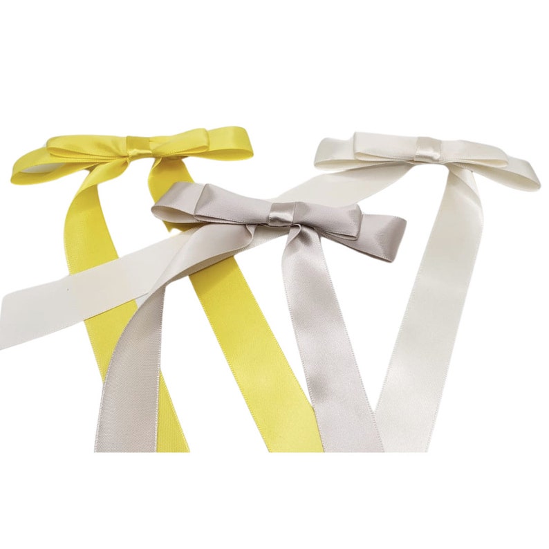 May include: Three satin ribbon bows in yellow, grey, and white. The bows are tied with long tails.