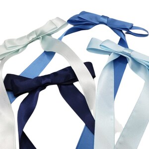 May include: Four satin ribbon bows in different shades of blue and white. The bows are tied with long tails and are ready to be used for decorating gifts or crafts.