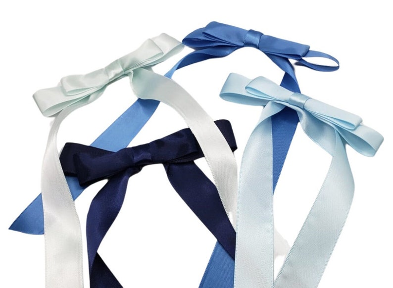 May include: Four satin ribbon bows in different shades of blue and white. The bows are tied with long tails and are ready to be used for decorating gifts or crafts.