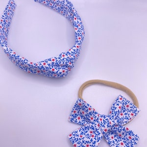 Könnte beinhalten: Ein weißes Stirnband und Schleifen-Set mit einem blauen Blumen- und roten Sternmuster. Das Stirnband ist oben geknotet. Die Schleife ist an einem hautfarbenen Gummiband befestigt.