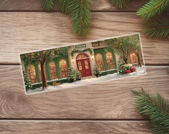 May include: A rectangular Christmas-themed bookmark featuring a bookstore scene. The bookstore has a red door, green trim, and snow on the ground. The windows are lit, and there are Christmas trees and presents. The word "Bookstore" is above the door.