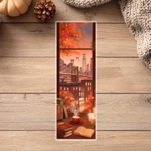 Peut inclure: Marque-page illustr&eacute; avec une vue sur un paysage urbain &agrave; travers une fen&ecirc;tre. La sc&egrave;ne comprend un pont, des b&acirc;timents et des feuillages d'automne. Une tasse de caf&eacute;, des livres et une bougie sont sur le rebord de la fen&ecirc;tre. La palette de couleurs est chaude, avec des tons orange, rouge et brun.