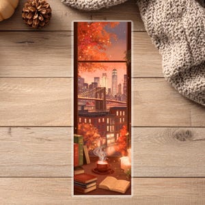 Peut inclure: Marque-page illustr&eacute; avec une vue de ville &agrave; travers une fen&ecirc;tre, avec un pont et des b&acirc;timents. Des feuilles d'automne encadrent la sc&egrave;ne. Une tasse de caf&eacute;, des livres et une bougie sont sur le rebord. La palette de couleurs est chaude, avec des tons orange, marron et rouge.