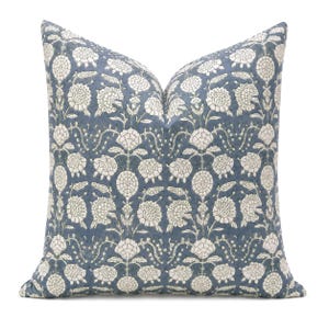 May include: A square throw pillow featuring a slate blue background with a repeating cream-colored floral pattern. The design consists of stylized flowers and leafy vines arranged in a symmetrical grid, creating a detailed botanical print.