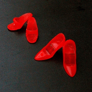May include: Four red plastic high heel shoes. The shoes are all different styles and sizes.