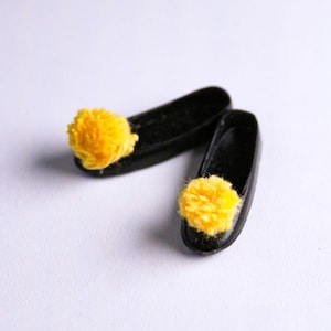 Pode incluir: Um par de chinelos pretos com pompons amarelos nos dedos.